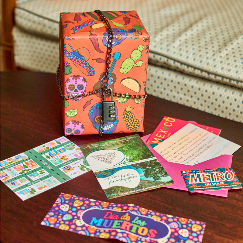 Padlock'd Mexico: a wrapped gift locked with a chain beside the envelope contents, including a metro ticket and a Day of the Dead card