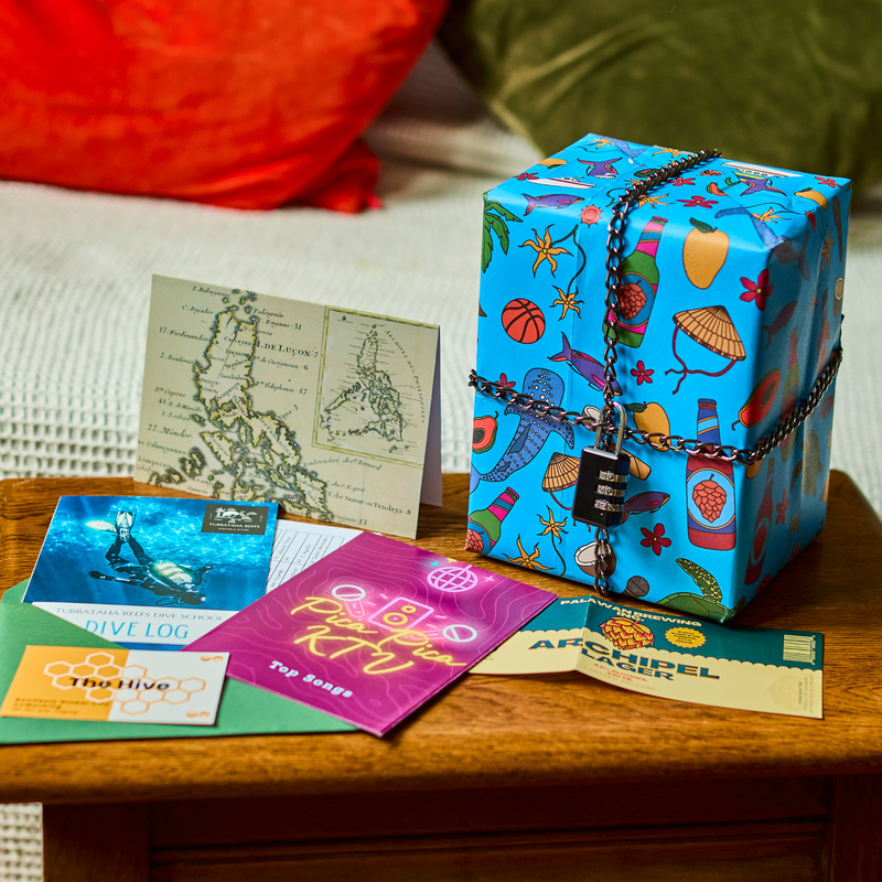 Padlock'd The Philippines: a blue patterned gift locked with a chain next to a map, a dive logbook and a karaoke song book